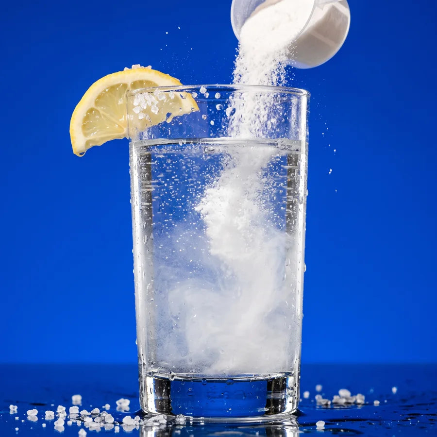 A scoop of Salty Creatine powder pouring into a glass of water with a lemon wedge